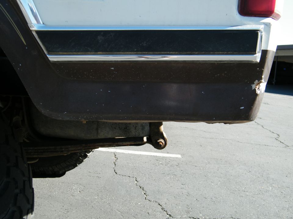 White vehicle's rear bumper and tire, showing dark trim and rust spots