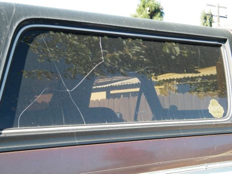1982 Ford Bronco - The side window of a vehicle shows extensive cracking, obscuring the view of the surroundings.