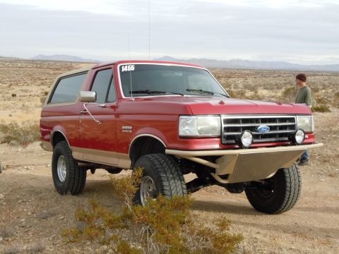 1982 Ford Bronco - This red Ford Bronco features a custom bumper and off-road tires, suggesting it's modified for terrain.