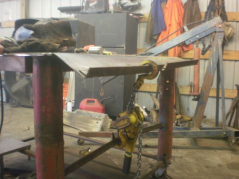 1995 Ford Bronco - A chain hoist is attached to a metal workbench, with various tools and equipment in the background of a workshop.