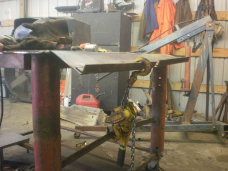 Engine hoist and chain attached to a metal workbench in a garage. Tools and equipment are visible in the background