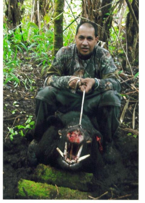 1991 Ford Bronco - A person in camouflage clothing crouches in a dense green forest, holding a hunted wild boar with prominent tusks. No vehicle or vehicle pa…