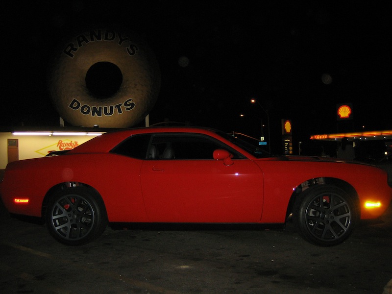 Red Dodge Challenger parked at night under the Randy's Donuts sign