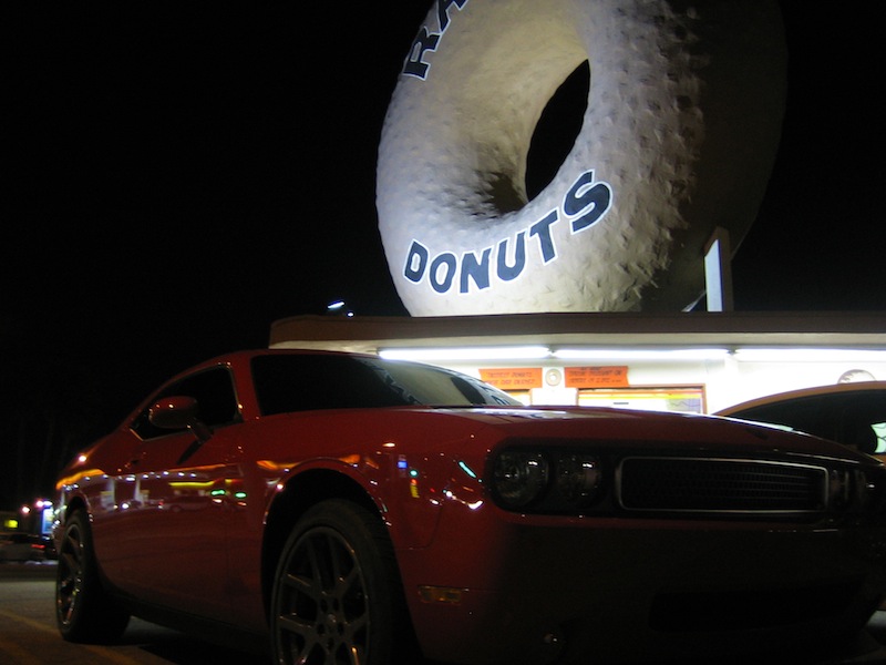 Low front angle of a red Dodge Challenger under the Randy's Donuts sign at night