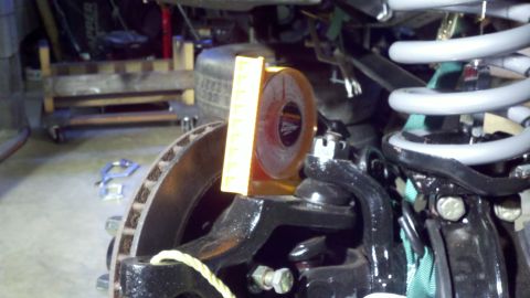 1995 Ford Bronco - Close-up of a front suspension corner in a garage, with a translucent orange Daystar polyurethane bump stop or spacer held against the coil…