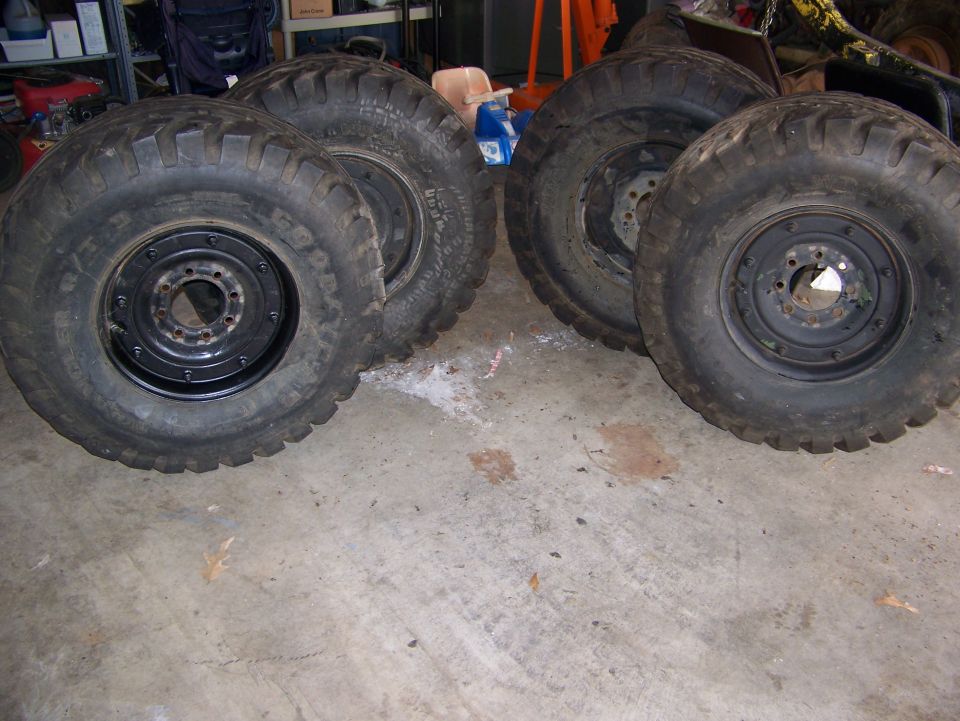 Set of four mud-terrain tires on black 8-lug steel wheels standing on a garage floor
