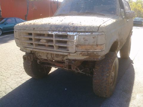 1995 Ford Bronco - This heavily mud-caked truck is shown from the front, with another vehicle in the background.