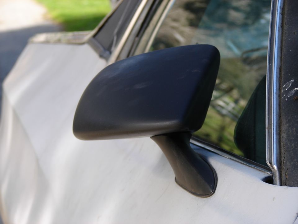 Black side mirror on a white vehicle, close-up side view