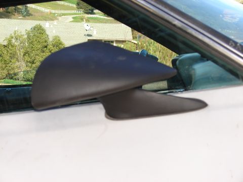 1973 Ford Ranchero - Close-up of an aftermarket side mirror on a white vehicle door, with a blurred background of houses and trees.