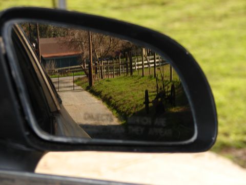 1973 Ford Ranchero - Reflection in a side mirror shows a driveway leading to a barn, bordered by a wooden fence and green grass.