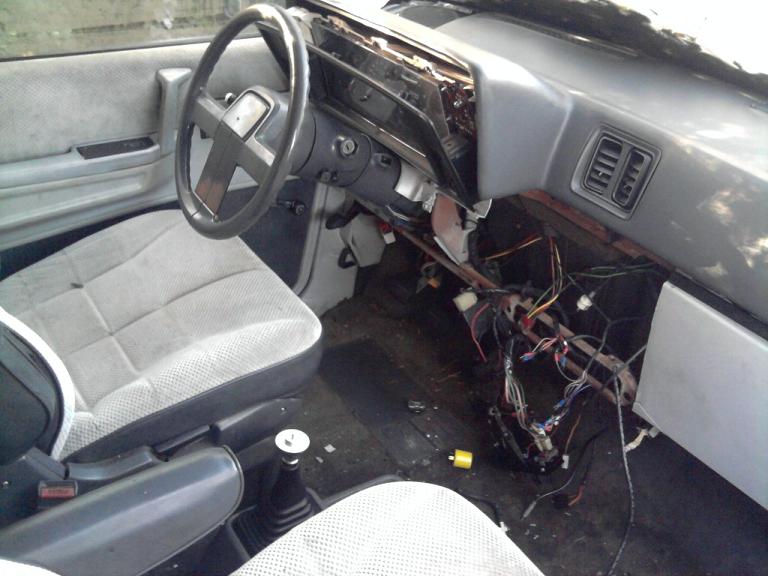 Car interior showing dashboard with wires pulled out and seats