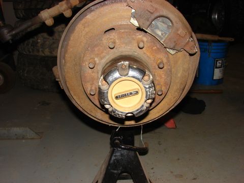 1971 International School Bus - Close-up of a heavily rusted wheel hub and brake assembly, resting on an automotive jack stand.