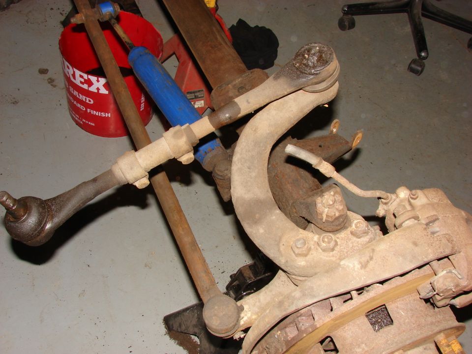 Worn steering knuckle, tie rod and components on a garage floor