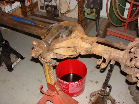1971 International School Bus - A vehicle's rear axle assembly is supported by jack stands, with a red bucket collecting fluid.
