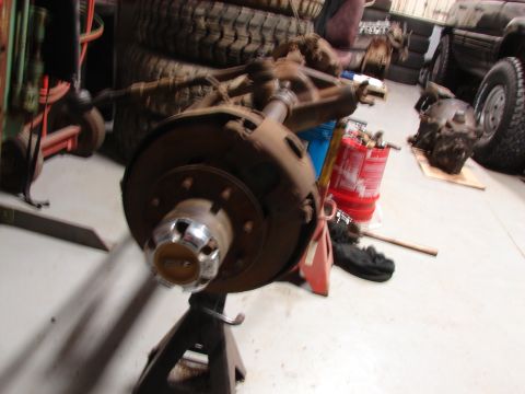 1971 International School Bus - Front axle assembly, likely from a heavy-duty truck, is supported by an engine stand in a garage setting.