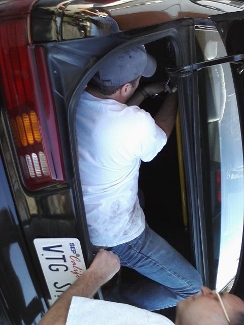 1995 Ford Taurus - Mechanic working on the interior of a dark-colored vehicle, with a license plate visible.