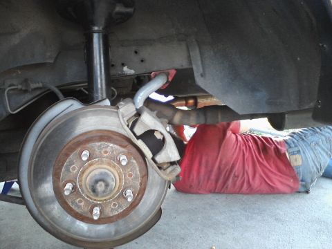 1995 Ford Taurus - A person works on the rear suspension and brake assembly of a vehicle.