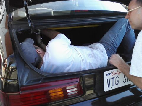 1995 Ford Taurus - Someone is working on something inside the trunk of a car while another person observes.