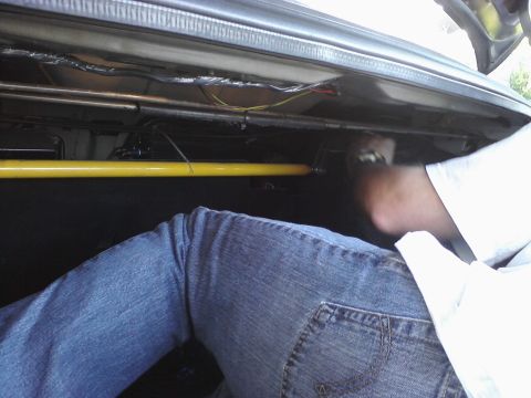 1995 Ford Taurus - Interior view of a car trunk, showing a yellow strut bar and wiring, with a person working inside.