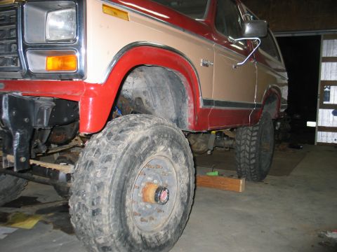 1984 Ford Bronco - Close-up of the front wheel well and fender of a tan and red Ford Bronco.