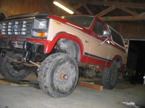 1984 Ford Bronco - This two-tone red and tan Ford Bronco is shown with its front end elevated, revealing its suspension and large off-road tires.