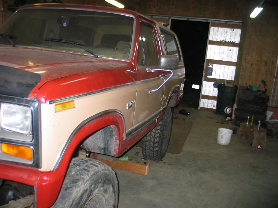 Red and tan Ford Bronco with lifted suspension, seen from the front quarter angle in a garage