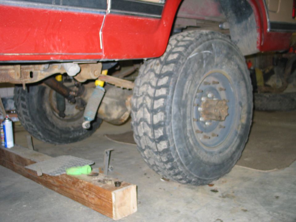 Underside of lifted red truck showing axle, shock and mud-terrain tires