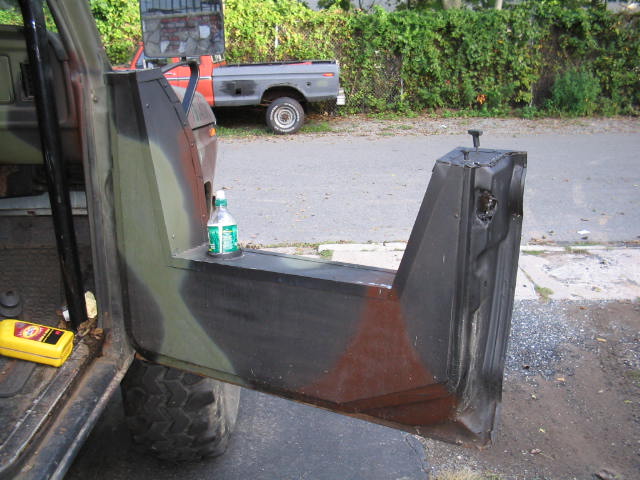 Camouflage half door open on a Bronco with a water bottle on it; red Ford pickup in background