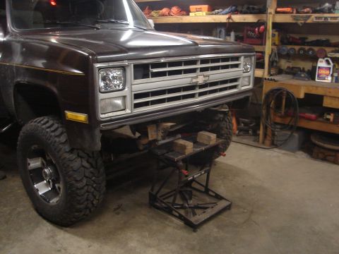 1989 Ford Bronco - Front driver-side corner of a dark brown square-body Chevrolet pickup lifted on mud-terrain tires and polished eight-lug wheels, its front…