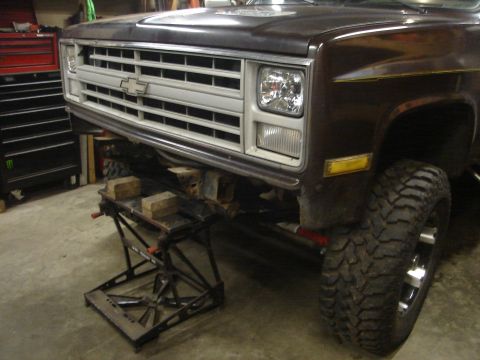 1989 Ford Bronco - Front view of a brown Chevrolet truck, lifted and supported by jack stands in a garage.
