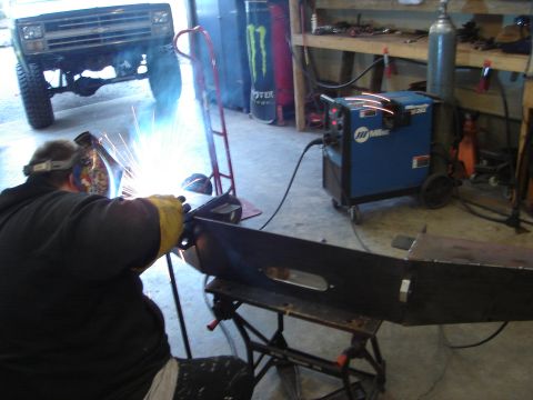 1989 Ford Bronco - A person welds a metal piece in a garage, with the front of a truck visible in the background.