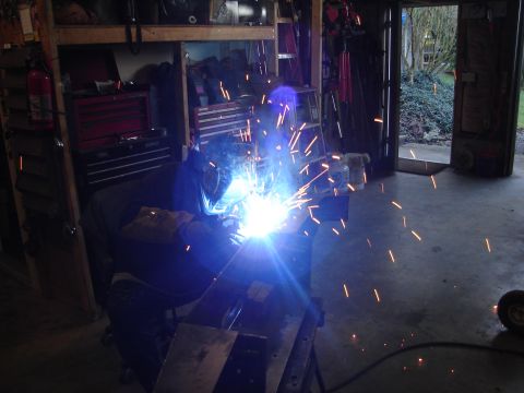 1989 Ford Bronco - A person is welding in a garage, with sparks illuminating the scene and tools visible on shelves.