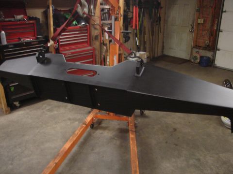 1989 Ford Bronco - A black metal component, possibly a skid plate or frame section, is supported by an engine stand in a workshop setting.