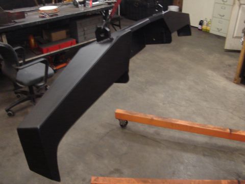 1989 Ford Bronco - A black metal bumper is shown in a workshop setting, resting on an engine hoist.