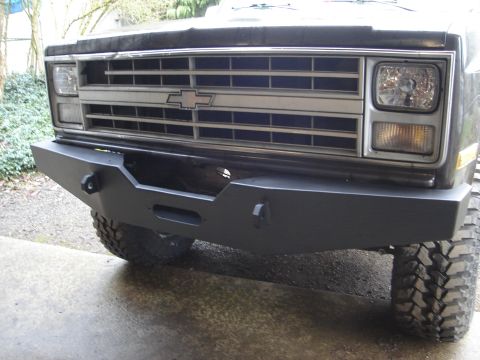 1989 Ford Bronco - The front grille and bumper of a Chevrolet truck are visible, with off-road tires on the front wheels.