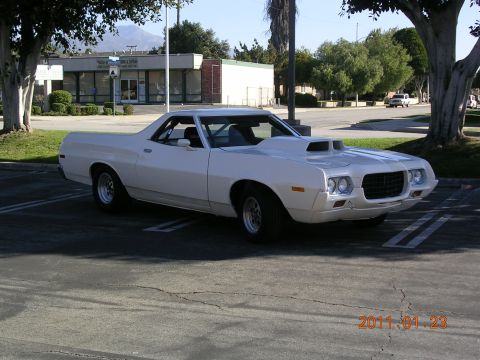 1972 Ford Ranchero - A white 1972 Ford Ranchero is parked in a lot, with a building and trees in the background.
