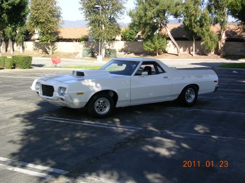 1972 Ford Ranchero - A white 1972 Ford Ranchero is parked in a lot, viewed from the front three-quarter angle, showing its distinctive hood scoop and custom whe…