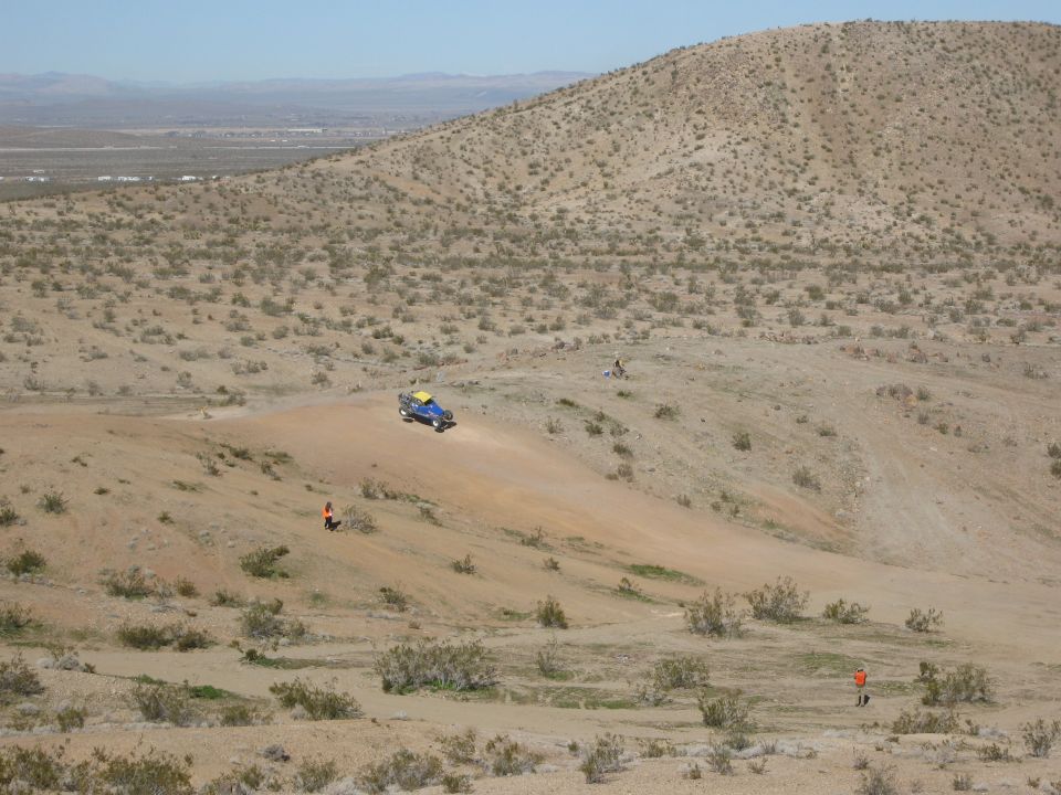 Blue off-road vehicle with yellow top driving on a dirt hill in a desert