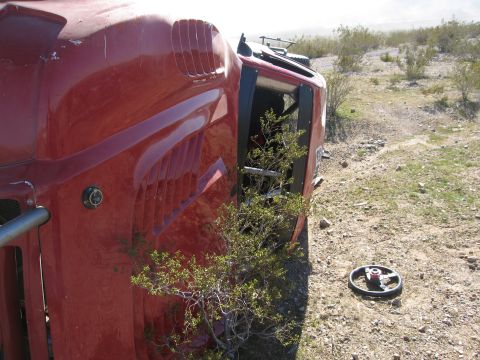 1986 Ford Bronco - A red vehicle lies overturned in a dry, brushy area, with vegetation growing inside the cab.