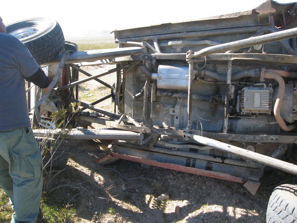 Rolled off-road truck on its side in the desert, underbody frame, exhaust and skid plate exposed