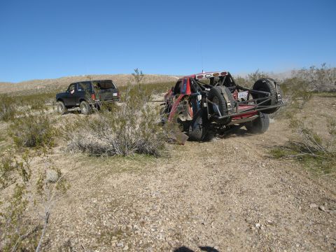 1986 Ford Bronco - Two off-road vehicles are seen in a desert environment under a clear blue sky.