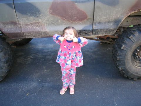 1979 Ford Bronco - A young child poses with a large, lifted truck, dwarfed by its massive tires.