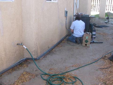 1968 Ford Mustang - A person is working on an outdoor air conditioning unit, with hoses and electrical conduit nearby.