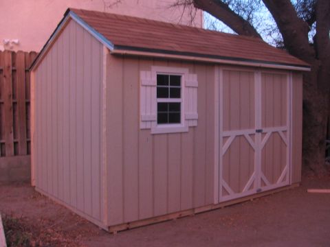 1968 Ford Mustang - A tan shed with a brown roof and white trim sits outdoors next to a wooden fence and a large tree.