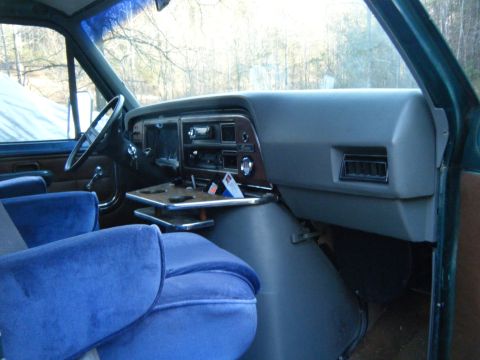 1981 Ford E350 - The interior of a van shows plush blue seats and a functional dashboard with a fold-out tray.