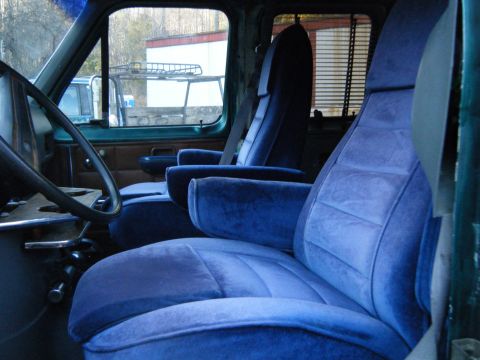 1981 Ford E350 - The interior of a van features plush blue velour seats and a view of the exterior through the windows.