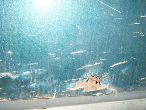 1981 Ford E350 - Close-up of rust and scratches on a teal vehicle panel, indicating wear and tear.