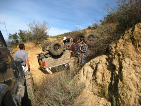 1989 Ford Bronco - A group of people are gathered around an overturned off-road vehicle on a steep, dusty incline.