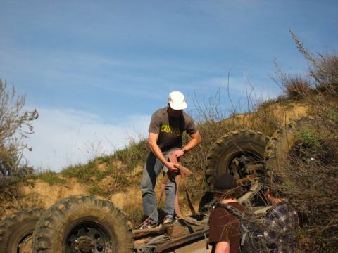 1989 Ford Bronco - A group of people attempt to recover an off-road vehicle that has tipped onto its side in a grassy, hilly area.