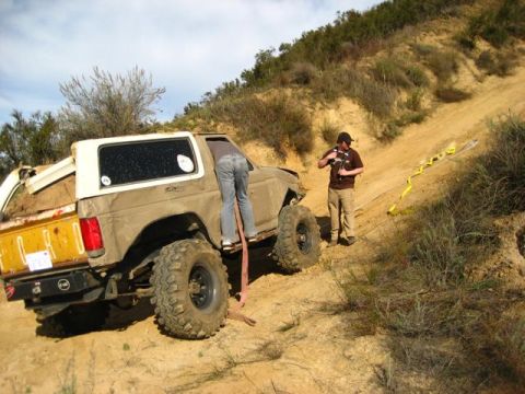 1989 Ford Bronco - A 1989 Ford Bronco is stuck on a steep dirt incline, with a person attempting to assist.